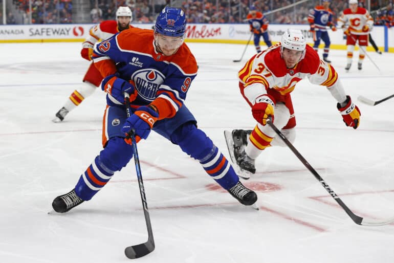 Sep 21, 2025; Edmonton, Alberta, CAN; Edmonton Oilers forward Vasily Podkolzin (92) protects the puck from Calgary Flames defensemen Yan Kuznetsov (37) during the first period at Rogers Place. Mandatory Credit: Perry Nelson-Imagn Images